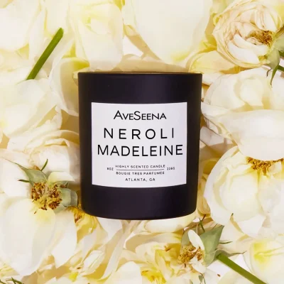 AveSeena Neroli Madeleine candle surrounded by soft white roses, highlighting its highly scented and luxurious design.
