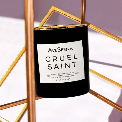 AveSeena Cruel Saint candle in sleek black container, surrounded by geometric gold decor, emphasizing luxury and wellness. Free shipping on all U.S. orders.