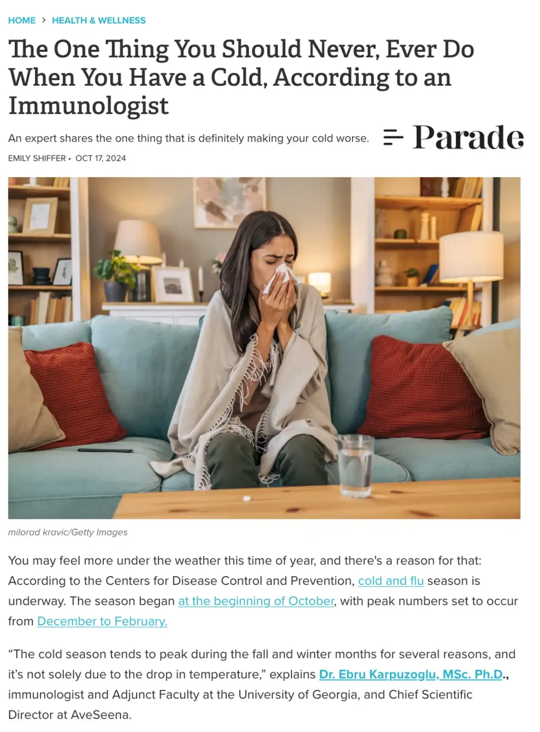 ParadeAveseena PARADE featuring Dr Ebru about one thing you should never do when you have a cold Woman sitting on a couch, wrapped in a blanket, holding a tissue to her nose, appearing unwell, with a glass of water and a phone on a wooden table, in a cozy living room setting.