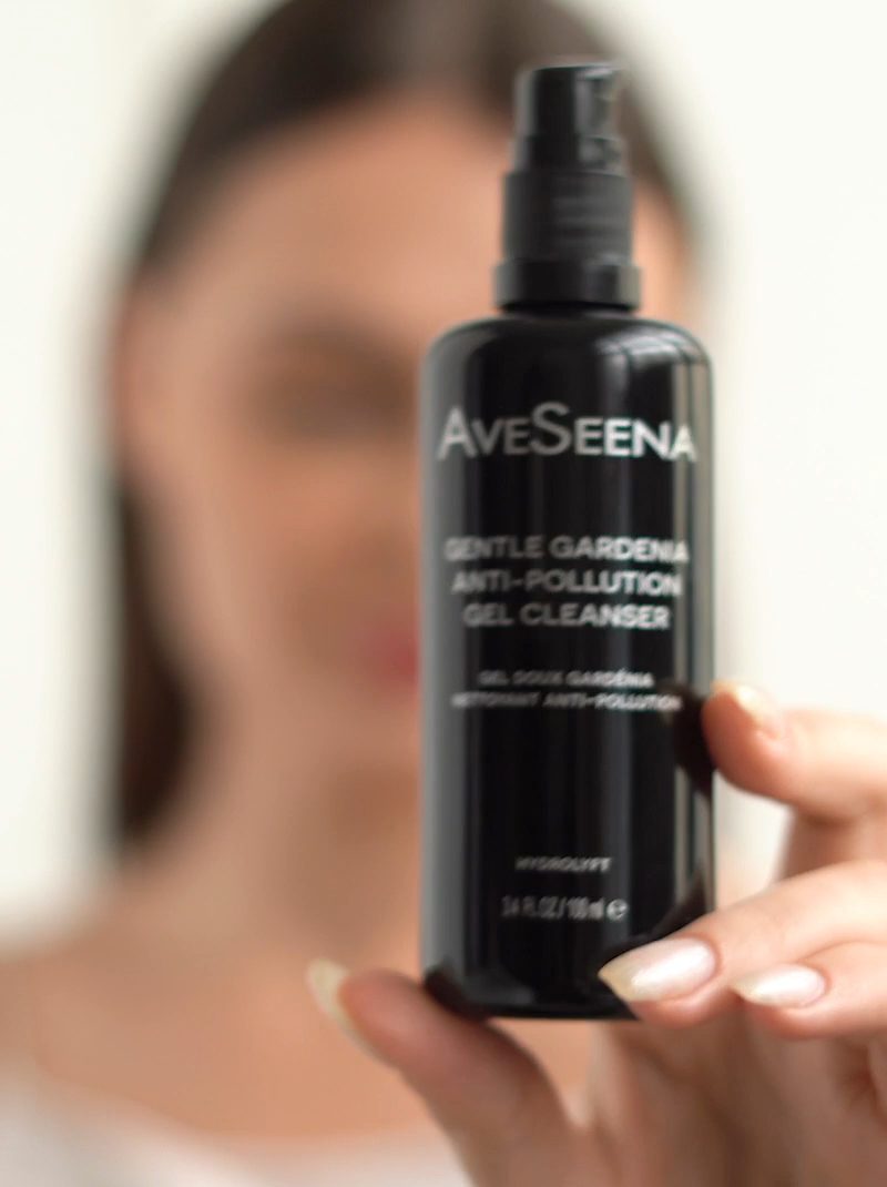 AVS_GGC_V-poster-1.jpeg Close-up of a hand holding a black bottle of AveSeena Gentle Gardenia Anti-Pollution Gel Cleanser. The background is softly blurred, focusing on the product.