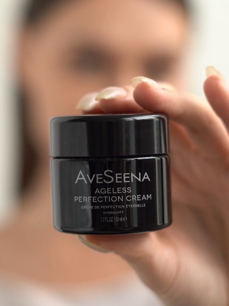 AVS_APC_Vs-poster-1.jpeg Close-up of a hand holding a black jar of "AveSeena Ageless Perfection Cream," with a blurred background, giving a refined and elegant tone.